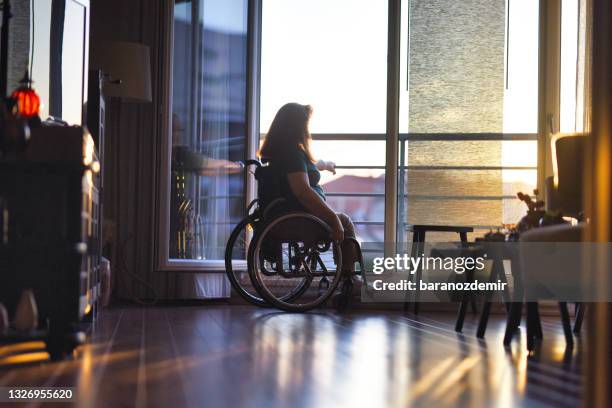 femme en fauteuil roulant devant la fenêtre ouverte de son appartement regardant le coucher du soleil - paraplegic woman photos et images de collection