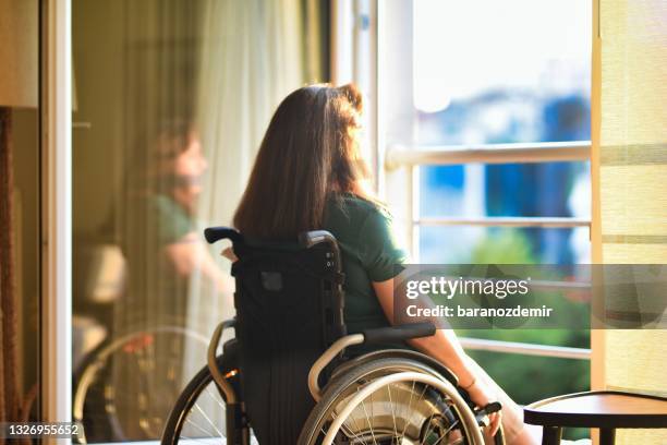 femme en fauteuil roulant devant la fenêtre ouverte de son appartement regardant le coucher du soleil - paralysie photos et images de collection