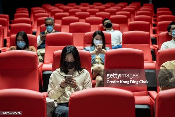 group of asian people wearing face mask sitting, using phone and waiting movie start at movie theater. - spectator mask stock pictures, royalty-free photos & images