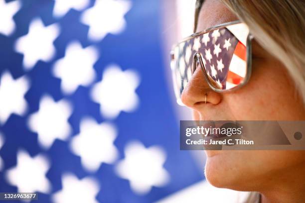 Fan looks on with an American flag reflected in her sunglasses during qualifying for the NASCAR Cup Series Jockey Made in America 250 Presented by...