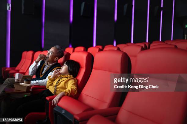 asian chinese grandfather and granddaughter sit on red seat in empty cinema theater, eating and watching movie - asian cinema bildbanksfoton och bilder