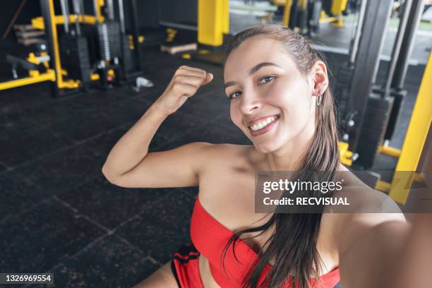 portrait of a beautiful smiling woman taking a selfie on her cell phone of her biceps at the gym - gym reopening stock pictures, royalty-free photos & images