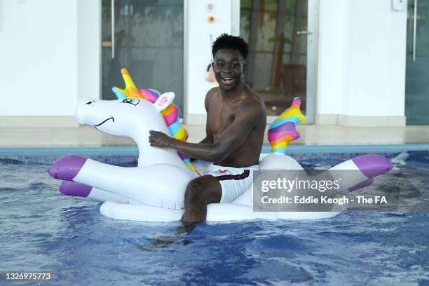 Bukayo Saka of England jumps into the swimming pool on an inflatable unicorn at St George's Park on July 04, 2021 in Burton upon Trent, England.