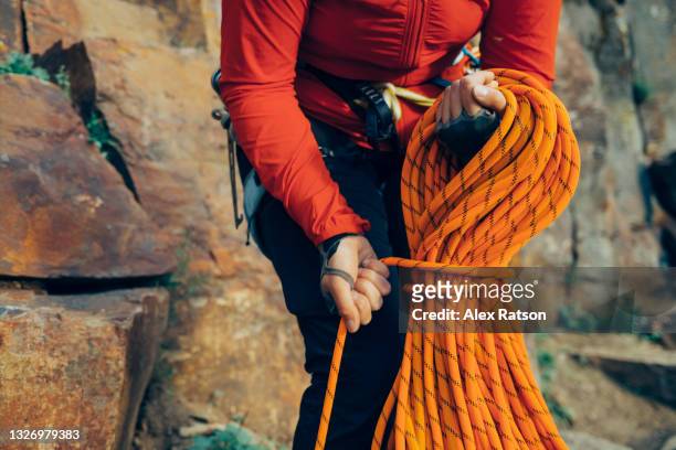 mountain climber coils a orange climbing rope and ties it off in preparation for putting it in a backpack - 爬山繩 個照片及圖片檔