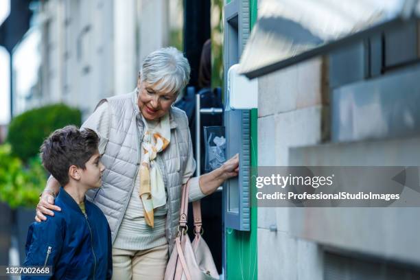 an older woman is withdrawing a cash from atm machine with her grandson. - grandma invoice stock pictures, royalty-free photos & images