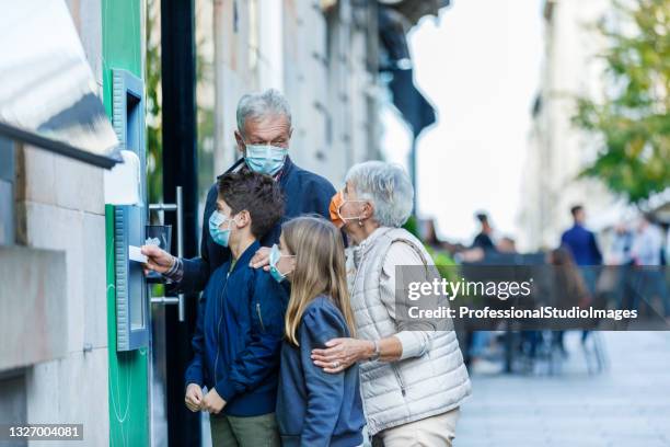 senior couple with grandson and granddaughter with face masks is using an atm machine. - grandma invoice stock pictures, royalty-free photos & images
