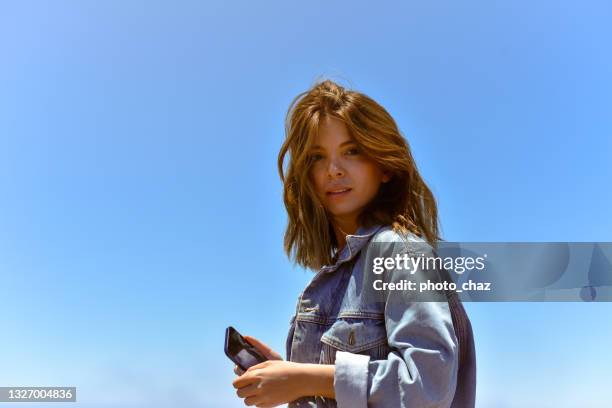 braunhaarige frau mit telefon in jeansjacke - blaue jacke stock-fotos und bilder