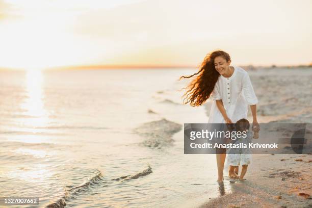 baby taking first steps on the beach, holding hands with mother. - baby lachen natur stock-fotos und bilder
