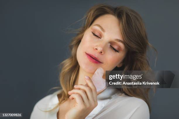 woman posing over grey background wall holding gua sha massage. - spooning stock pictures, royalty-free photos & images