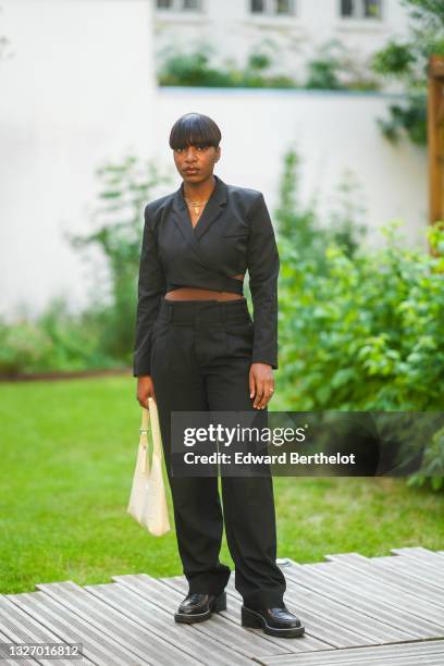 Loïcka Grâce wears a cropped black blazer jacket, black matching suit pants, black leather shoes, a golden nekclace, a bag, during the Twilly By...