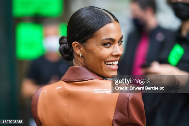 Tina Kunakey wears silver and gold earrings, a camel shiny leather long coat from Off-White with brown yoke on the back, attends the Off-White...