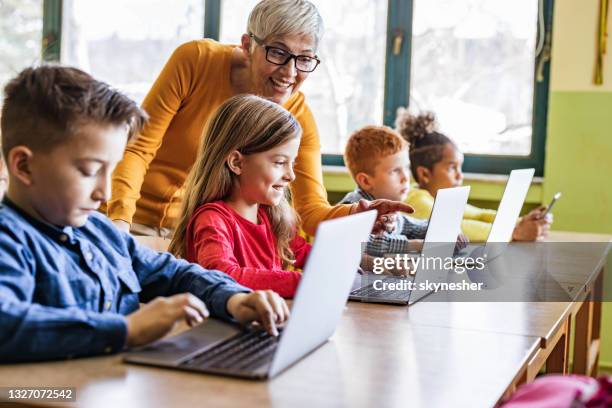 feliz maestra madura ayudando a sus estudiantes en la clase de computación en la escuela. - niño-en-edad-escolar fotografías e imágenes de stock