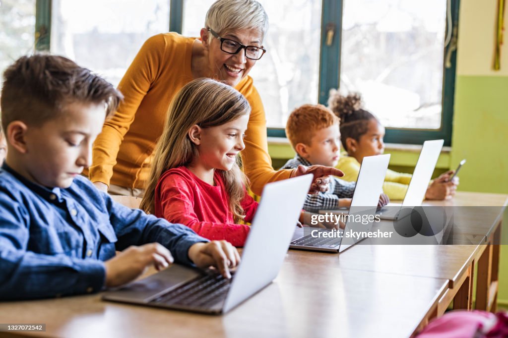 Insegnante matura felice che assiste i suoi studenti in classe di computer a scuola.