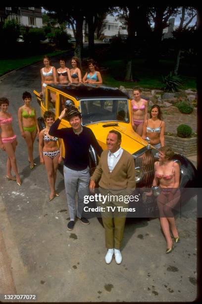 Entertainers Max Bygraves and Dickie Henderson alongside a classic car and a troupe of bikini-clad women, circa 1969.