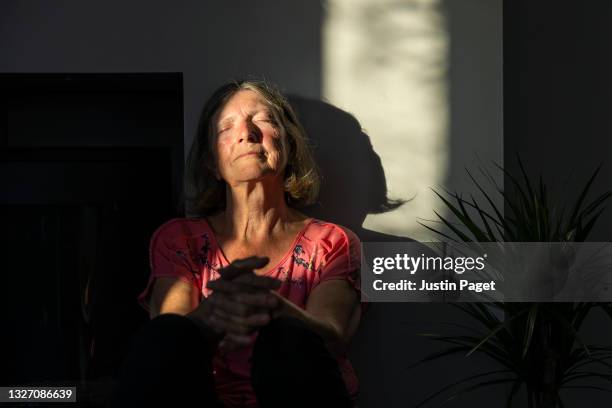 senior lady catching the last of the sun's rays in her home - shadow people fitness stockfoto's en -beelden