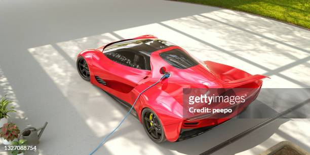 red electric sports car plugged into electric charger on driveway - red car wire stock pictures, royalty-free photos & images