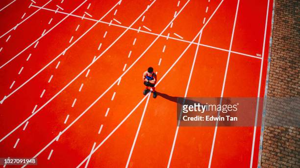 directly above drone point of view male asian chinese athlete standing at starting line arms crossed at track and field stadium - forward athlete stock pictures, royalty-free photos & images