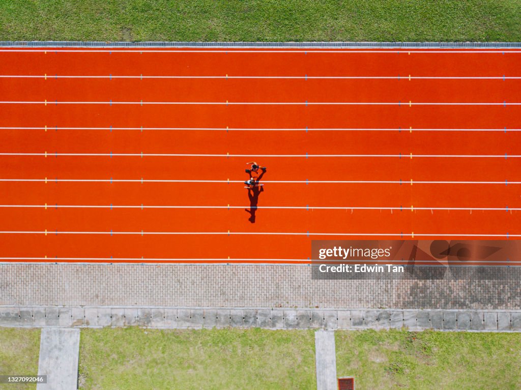 Directly above drone point of view Asian chinese father son running at track and run towards finishing line in the morning at track and field stadium beside bleachers