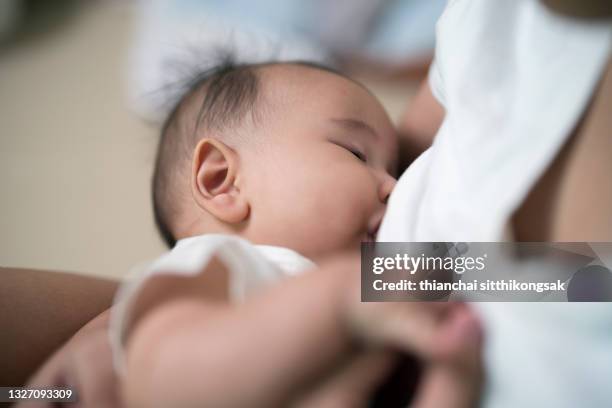 close-up of mother breastfeeding baby boy while sitting in living room at home . - breastfeeding stock pictures, royalty-free photos & images