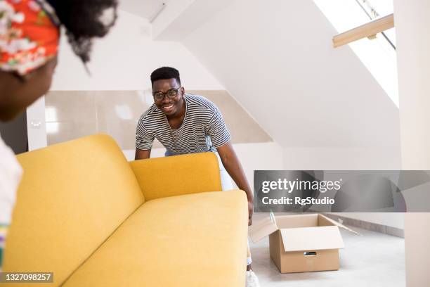 happy african american man and his wife carrying a new sofa into their new home - arrange stockfoto's en -beelden