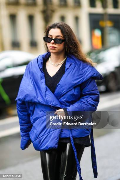 Guest wears black sunglasses, a gold earring, a pearls pendant necklace, a black V-neck wool pullover, black shiny leather pants, a royal blue shiny...