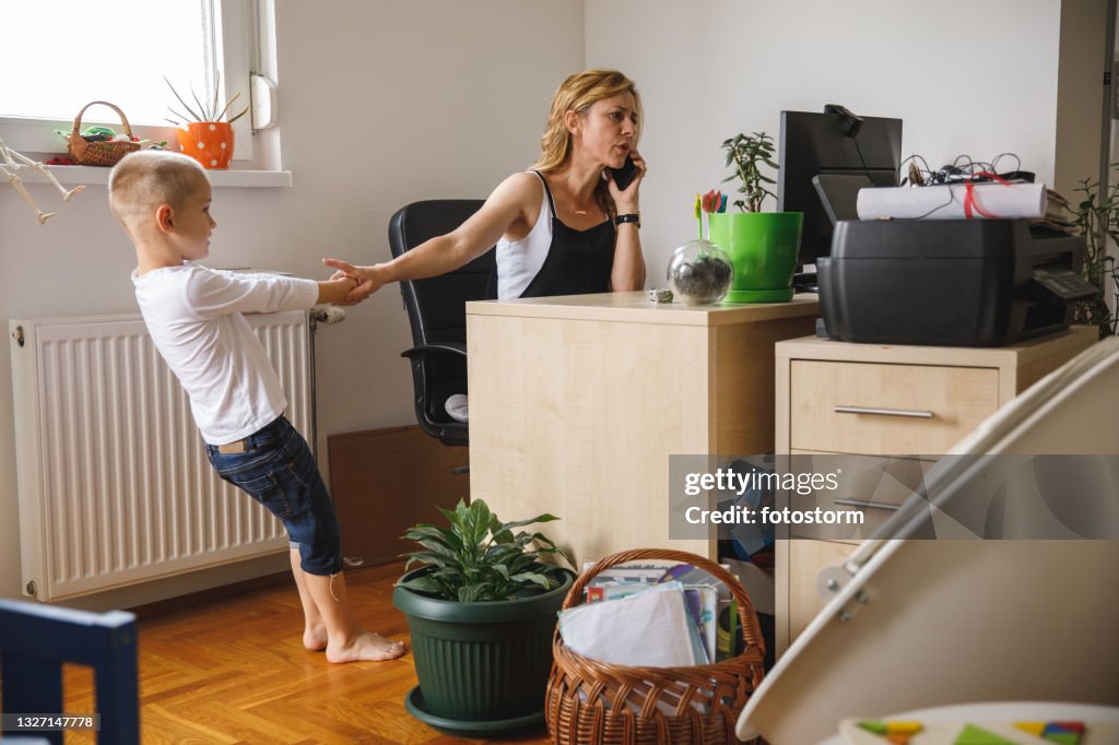 Boy pulling his mother's hand while she is on a conference call