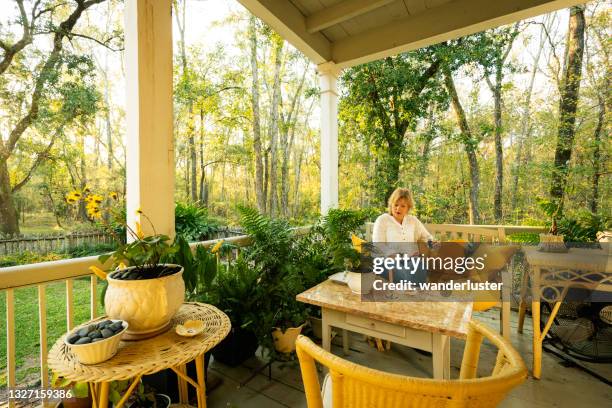 female tourist sits on the relaxing porch during an overnight stay at maison madeleine, a restored 1840's french creole cottage on the edge of lake martin swamp, lafayette, breaux bridge, louisiana - veranda maison stockfoto's en -beelden