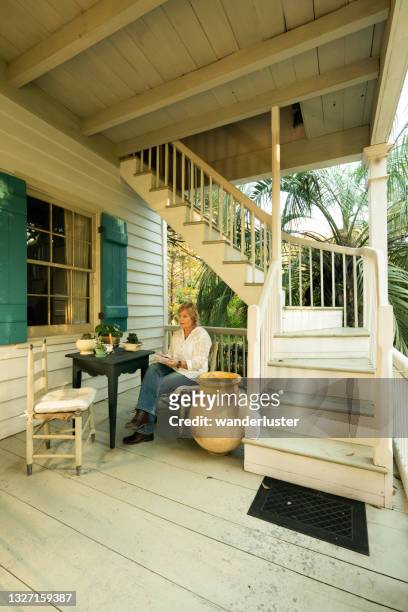 weibliche touristen sitzen auf der entspannenden veranda während einer übernachtung im maison madeleine, einem restaurierten französischen kreolischen cottage aus dem jahr 1840 am rande des lake martin sumpfes, lafayette, breaux bridge, louisiana - lafayette louisiana stock-fotos und bilder