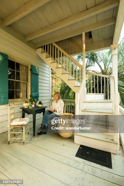 female tourist sits on the relaxing porch during an overnight stay at maison madeleine, a restored 1840's french creole cottage on the edge of lake martin swamp, lafayette, breaux bridge, louisiana - lafayette luisiana imagens e fotografias de stock