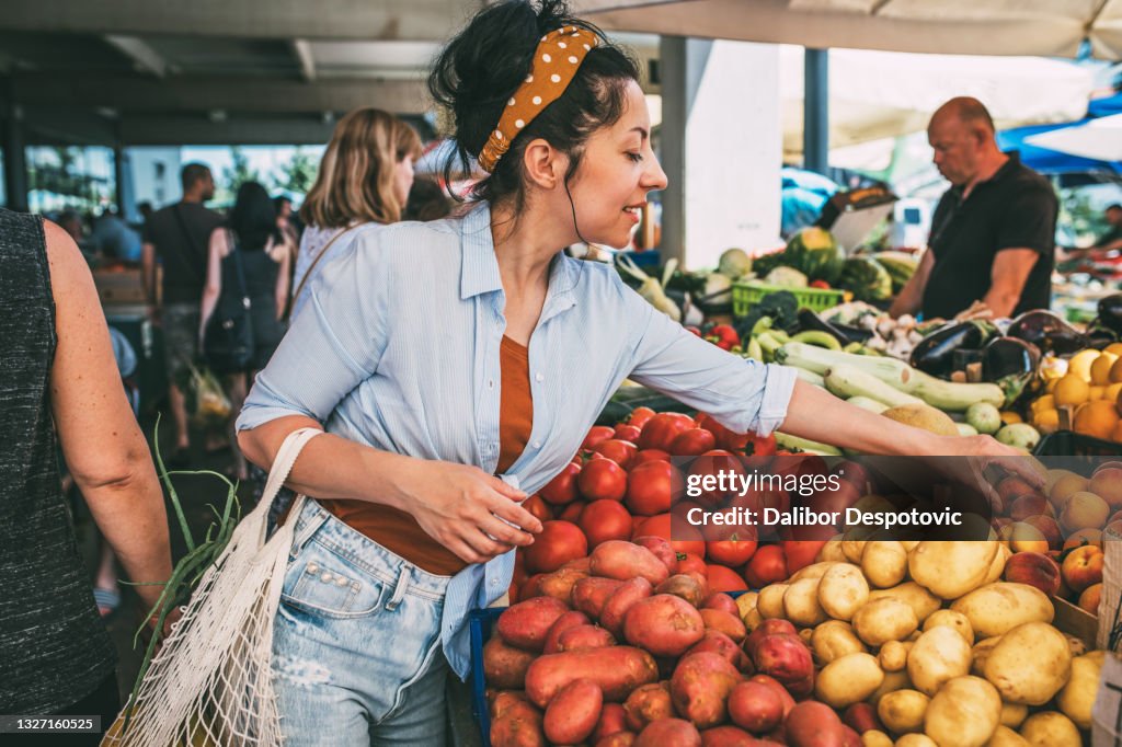 A young woman buys vegetables and fruits at the market .