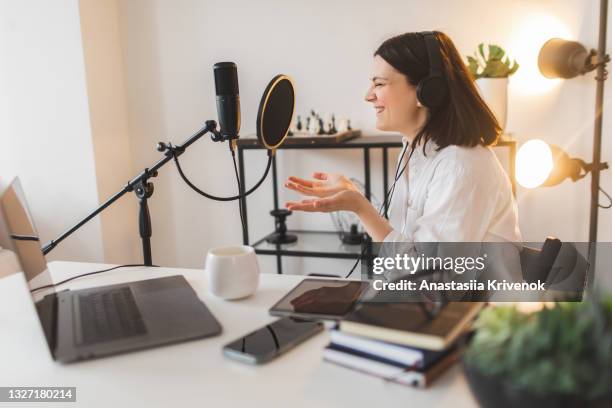 woman speaking expressively with hand gestures into a microphone at work desk - mujer feliz sola 30 35 fotografías e imágenes de stock