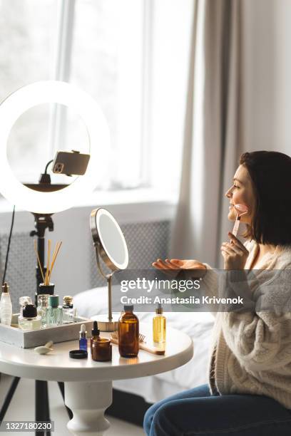 woman sitting at a table giving herself a face massage with a rose quartz roller. - mobile massage table stock pictures, royalty-free photos & images