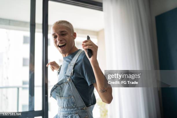 excited young man singing and dancing at home - hispanic gay man stock pictures, royalty-free photos & images