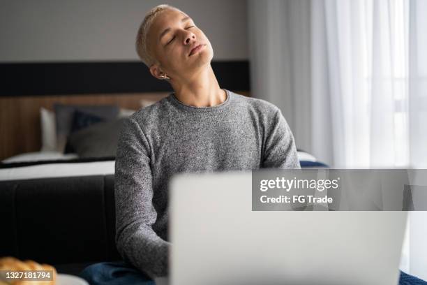 young man using laptop and stretching neck at home - neck stretch stock pictures, royalty-free photos & images