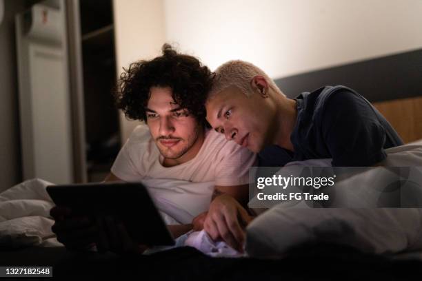 young gay couple using digital tablet on bed at home - watching ipad stock pictures, royalty-free photos & images