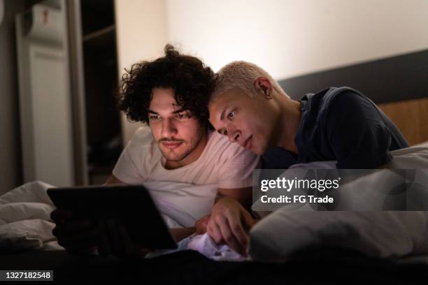 young gay couple using digital tablet on bed at home - young couple at movie together imagens e fotografias de stock