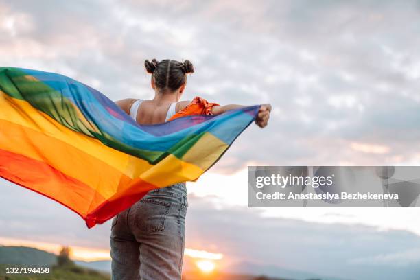 diversity girl standing back and holding rainbow flag on sky background - homocultuur stockfoto's en -beelden