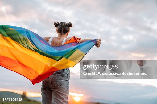 Diversity Girl standing back and holding rainbow flag on sky background Diversity Girl standing back and holding rainbow flag on sky background