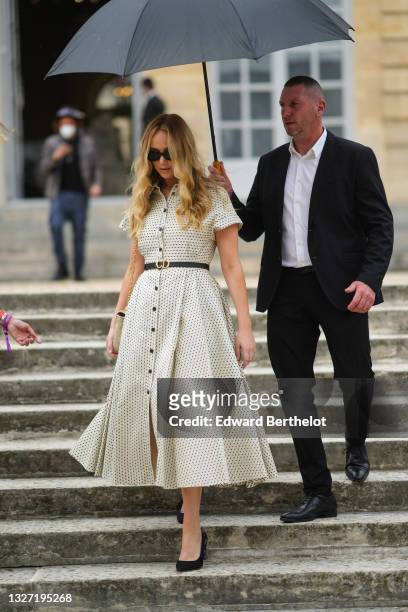 Jennifer Lawrence wears sunglasses, a midi dress with buttons, printed polka dots, short sleeves, a thin leather Dior belt, a Diot bag, outside Dior,...