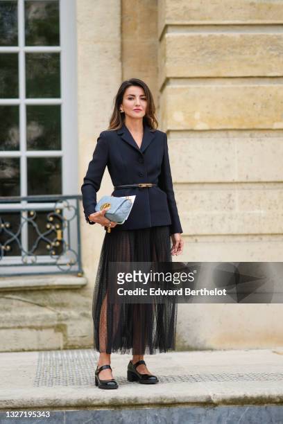 Alexandra Pereira wears a black blazer jacket with shoulder pads, a black leather thin belt, a pale blue quilted leather Dior bag, black pleated mesh...