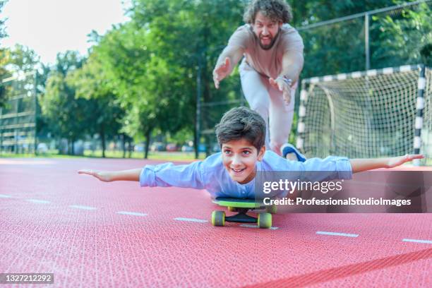 happy father is helping his son to learn to ride a long board. - father longboard stock pictures, royalty-free photos & images