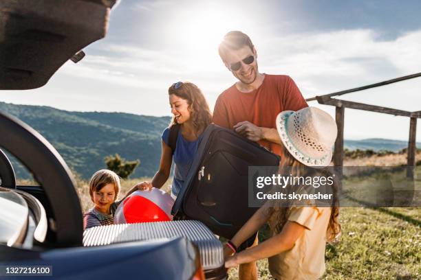 happy family talking while packing their luggage into a car trunk. - family luggage stock pictures, royalty-free photos & images