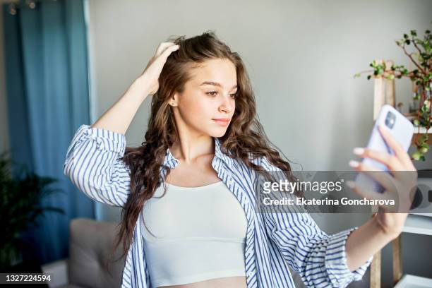 a beautiful young girl takes a selfie at home, takes pictures on her phone - girl selfie stock pictures, royalty-free photos & images