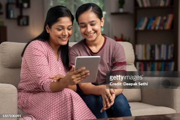 shot of a mother and daughter using digital tablet sitting on sofa at home:- stock photo - indian subcontinent ethnicity stockfoto's en -beelden