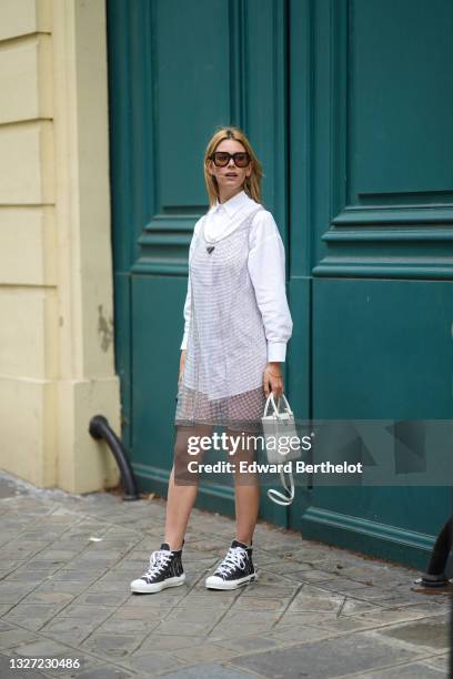 Natalia Verza wears black sunglasses, gold earrings, a white shirt, a silver pearls tank-top short dress from Prada, a gold bracelet, a white matte...