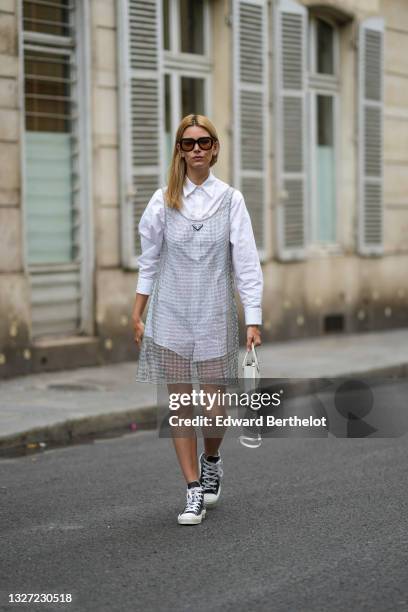 Natalia Verza wears black sunglasses, gold earrings, a white shirt, a silver pearls tank-top short dress from Prada, a gold bracelet, a white matte...