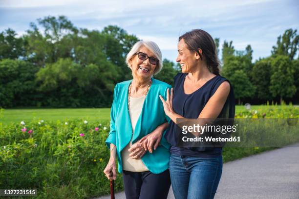 caring mid-adult woman with senior woman walking in park - generationsunterschied stock-fotos und bilder