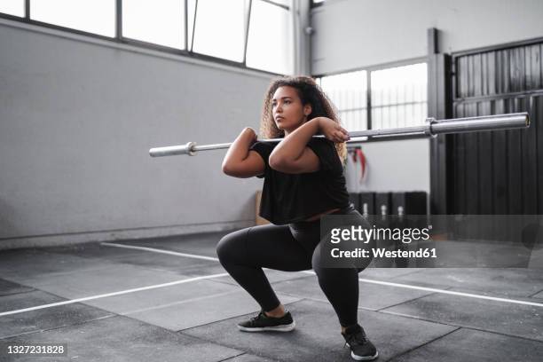 curly haired young woman practicing squats in gym - hockend stock-fotos und bilder