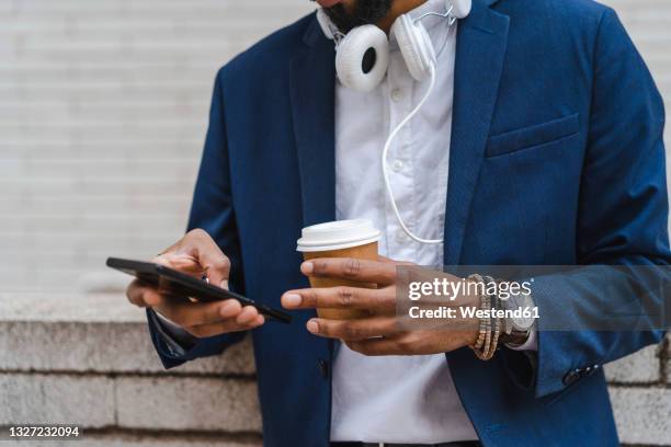 businessman holding disposable cup while using mobile phone in front of wall - midsection stock pictures, royalty-free photos & images