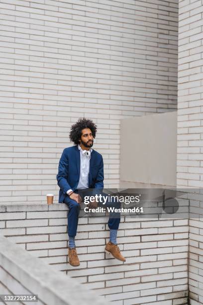 male entrepreneur contemplating while sitting on brick retaining wall - sitting on wall stock-fotos und bilder